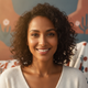 Smiling woman, late 20s to early 30s, looking confidently at the camera with a warm, approachable expression. Blurred natural